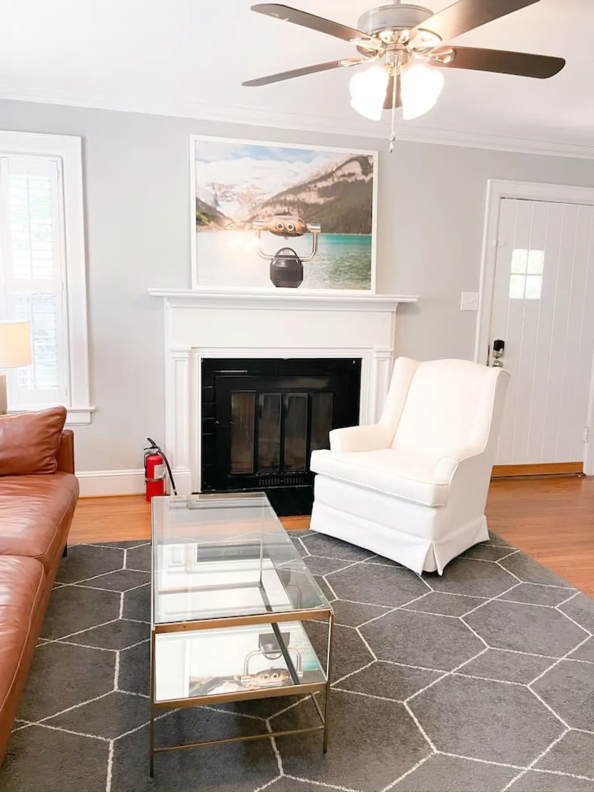 A cozy, open-concept living room featuring a comfortable leather sofa, a sleek glass coffee table, a white armchair, a modern fireplace, and artsy wall décor. The room is filled with natural light, creating a welcoming atmosphere for relaxation, socializing, or entertainment.